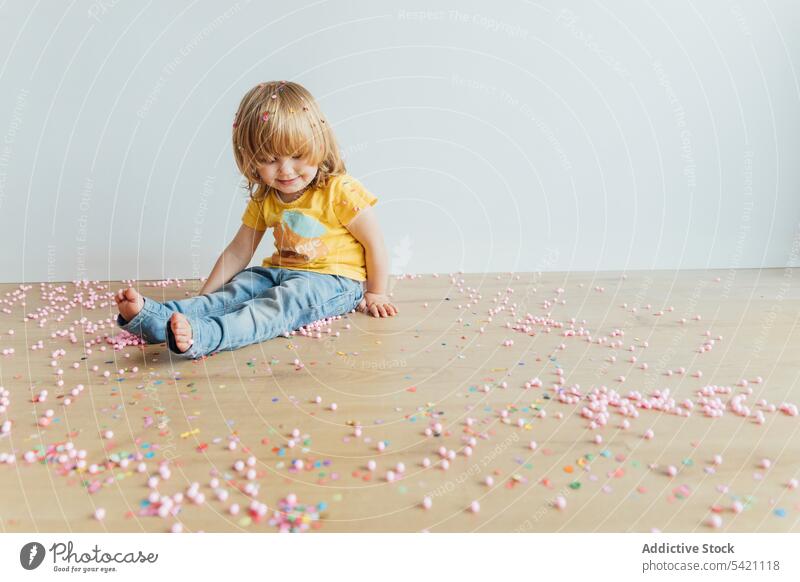 Cheerful kid having fun with colorful sprinkles play happy confetti messy preschool cheerful joy little small bead floor child childhood adorable playful cute