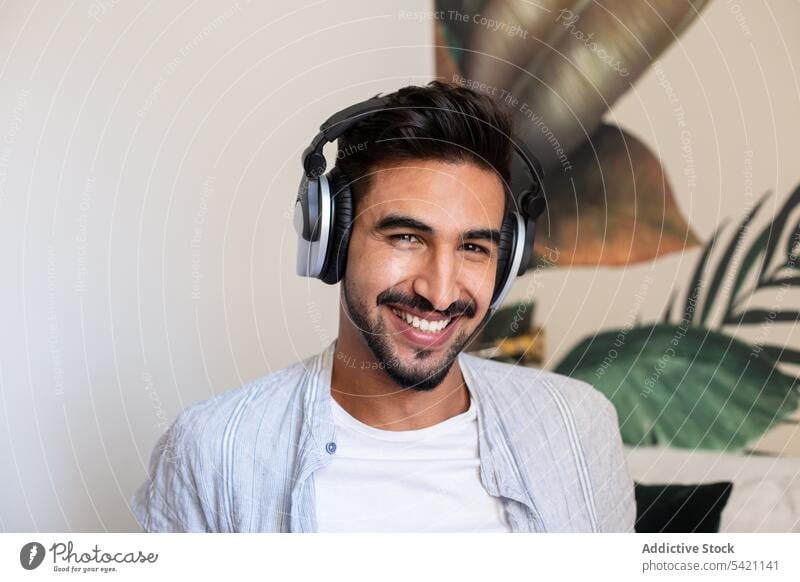 Bearded man listening to music and looking at camera smile home headphones ethnic happy rest weekend male headset cheerful sound beard fun cozy audio cool