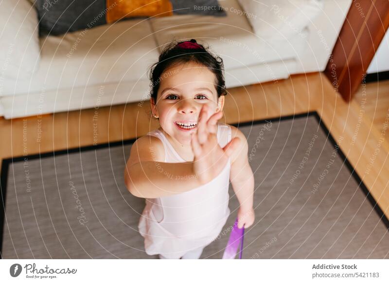 Happy little gymnast waving hand girl training home wave hand smile greeting ribbon leotard gymnastic rhythmic cheerful childhood sport gesture kid dancer