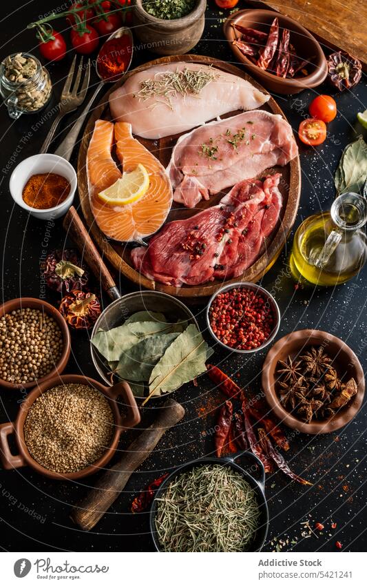 Flat lay of proteins surrounded by spices and seasonings on table product meat salmon condiment fish fillet food pepper cutting board spoon aromatic assorted