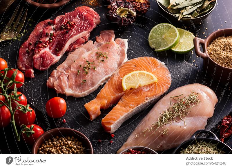 Flat lay of proteins surrounded by spices and seasonings on table product meat salmon condiment fish fillet food pepper cutting board spoon aromatic assorted