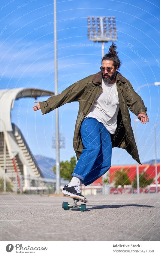 A Man skating on a skateboard on the road with his raincoat and sunglasses city guy sports people concrete urban asphalt recreation sunny skateboarding street