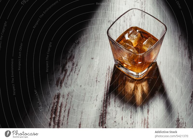 Glass of scotch in rays on aged rustic table in darkness glass whiskey bourbon alcohol beverage ice drink liquid liquor cognac brandy transparent fluid pour