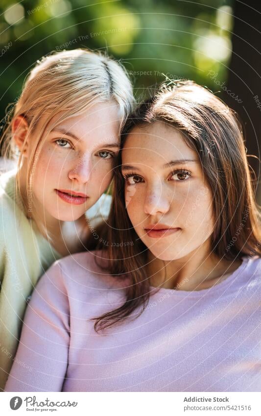 Charming teenage sisters looking at camera in park tender charming appearance together delicate girl garden nature summer sunny sunlight enjoy carefree harmony