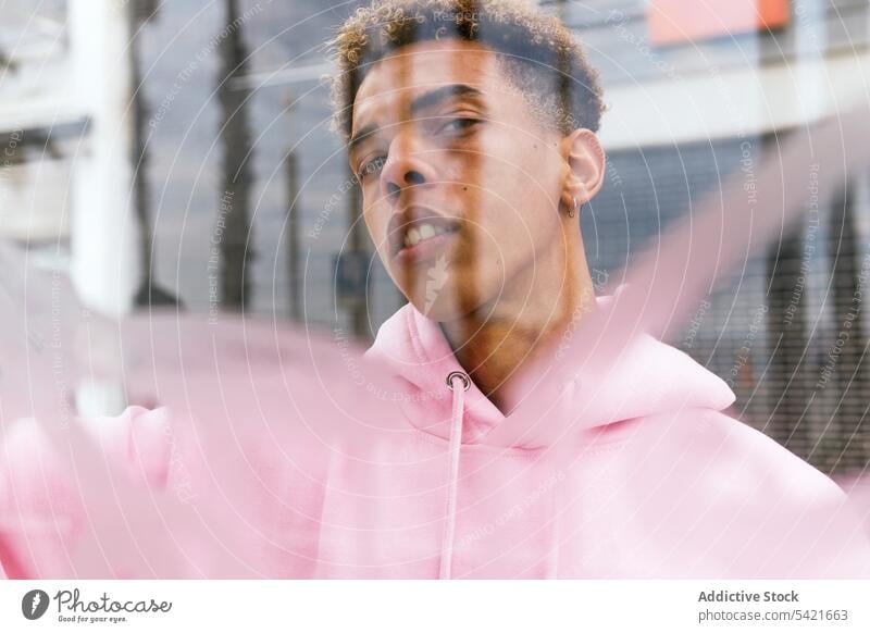 Informal ethnic man near window informal hipster independent style glass urban concept attitude hoodie alternative male modern confident afro pink millennial