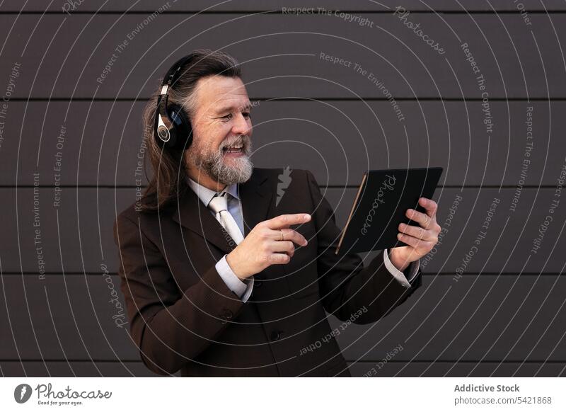 Happy mature businessman with headphones and tablet digital online communicate listen gadget using happy style middle age gray hair beard aged device internet