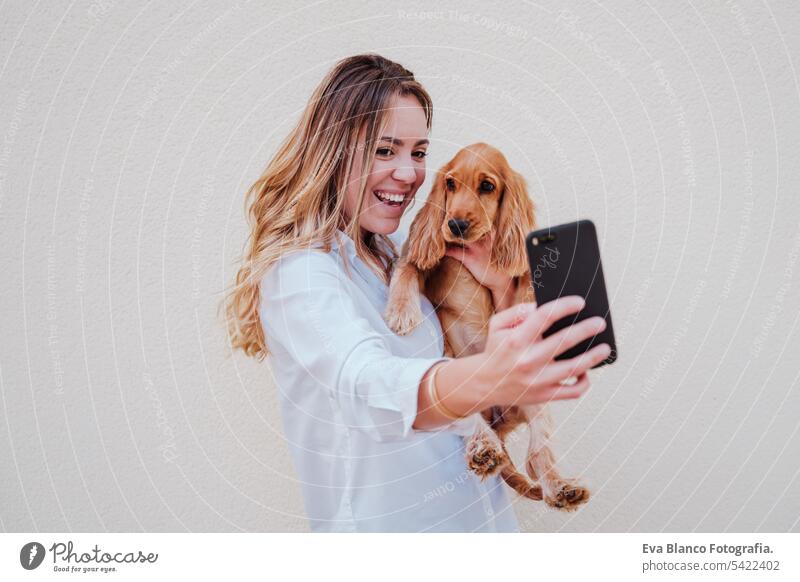 young woman at the street with her cocker dog taking a picture with mobile phone. Lifestyle outdoors with pets technology selfie friendship city beautiful