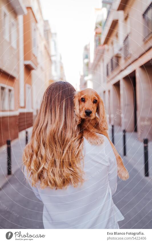 young woman at the street holding with her cute cocker dog on shoulder. Lifestyle outdoors with pets walking city urban purebred caucasian coker lifestyle