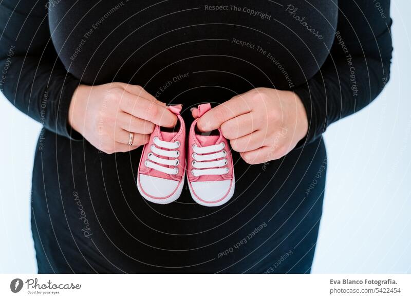 young pregnant woman home holding tiny pink baby shoes. family concept. close up motherhood parenthood expecting pregnancy indoor love touching newborn