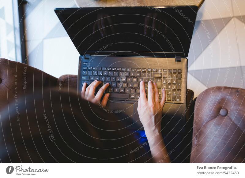 top view of a young beautiful woman writing on laptop, coffee besides. Casual blue dress. Modern life indoors hipster college computer display notebook looking