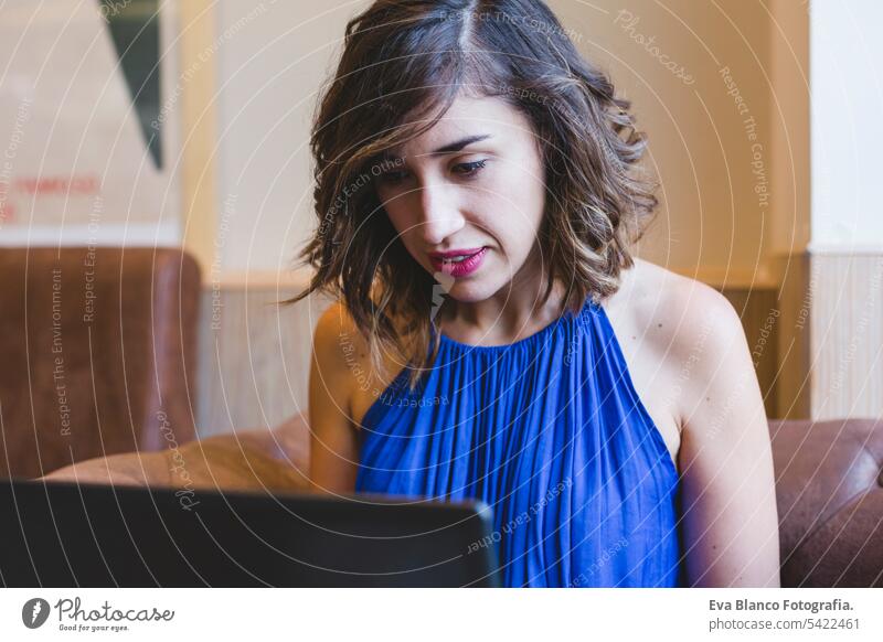 young beautiful woman working on laptop. she is wearing a casual blue dress. indoors modern lifestyle hipster college computer display notebook looking people