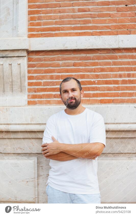 millennial guy with beard in white t-shirt standing near red brick wall man Brick wall Bearded man bearded millennials millennial generation handsome young Man