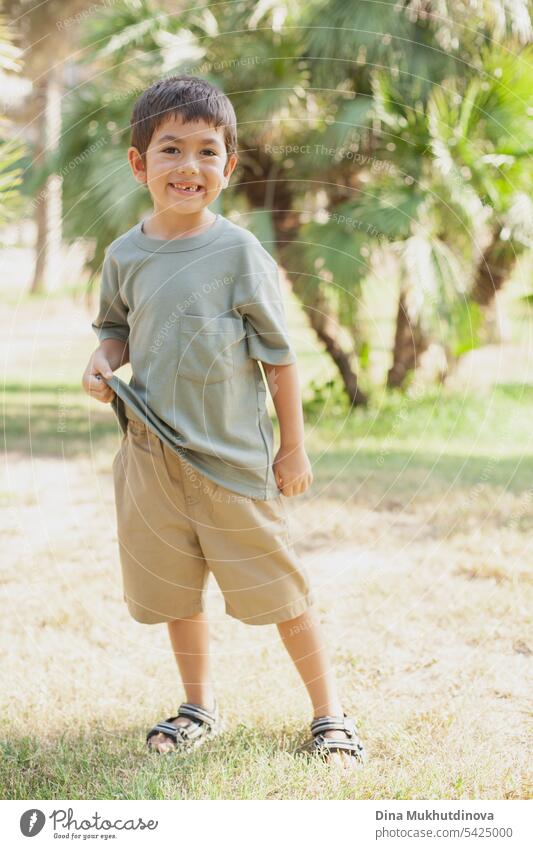 diverse kid standing in the park, smiling and looking to the camera. Five or six years old boy in the park in summer with palm trees as background. child