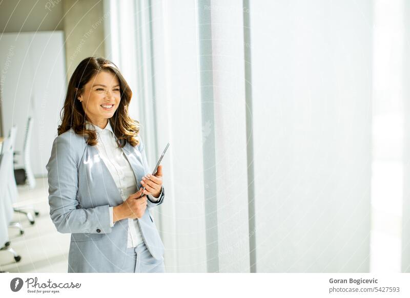 Young woman working on digital tablet by the office window adult alone attractive beautiful beauty bright brunette business business person businesspeople