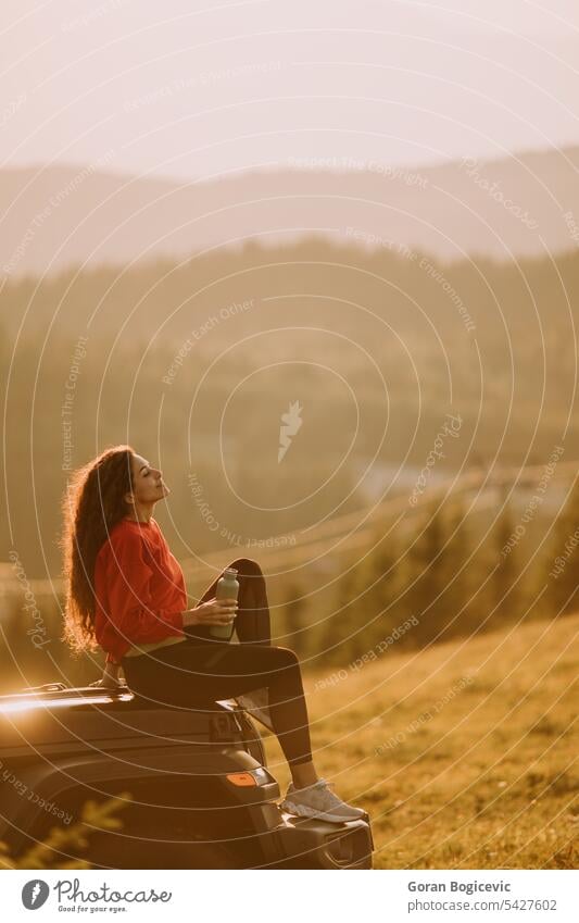 Young woman relaxing on a terrain vehicle hood at countryside adult adventure attractive auto automobile beautiful break calm car caucasian day drink drinking