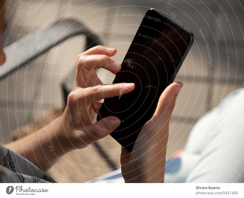 The hands of a young woman, using a smartphone sitting on a bench outside, in a park technology mobile digital screen person device communication business