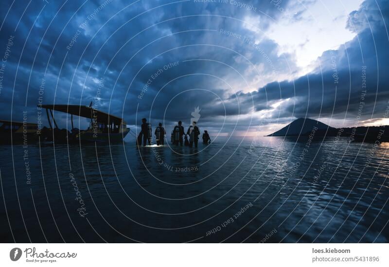 Divers walking into the ocean during sunset for a night dive in Bunaken, Sulawesi, Indonesia diver nature water sea diving flashlight bunaken indonesia sky fins