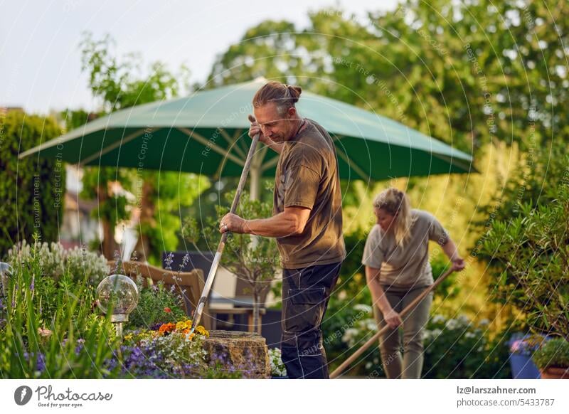 Male gardener raking the the flower bed while the collegue is sweeping the terrace in summer artisan builder concept confident copy space craft craftsman