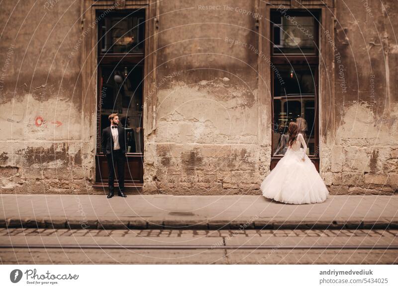 Happy newlywed couple on a walk in old European town street, gorgeous bride in white wedding dress together with handsome groom happy european love city woman