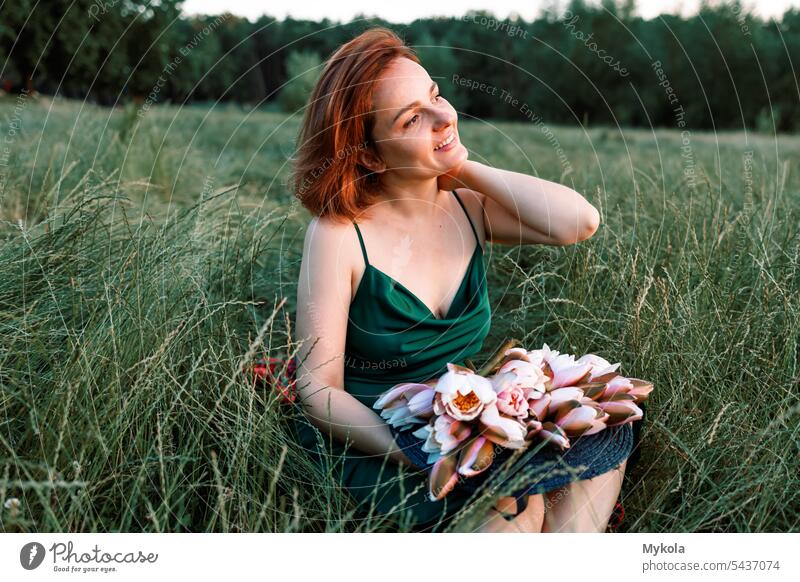 woman, resting  in the green grass, in a long green dress, and a pleasant smile on her face, holding flowers in her hands , enjoying harmony with nature and recuperating