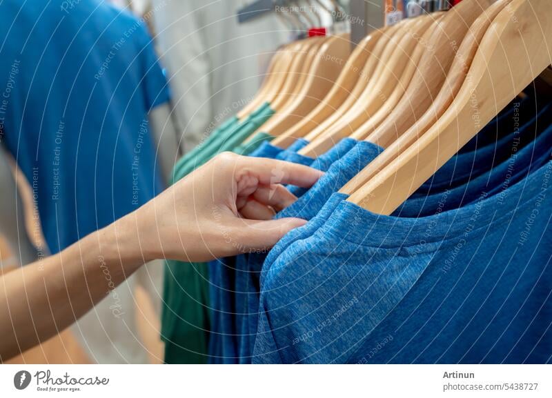 Woman shopping shirt in clothing store. Woman choosing clothes. Shirt on hanger hanging on rack in clothing store. Fashion retail shop inside shopping mall. Clothes on hangers in a clothes shop.