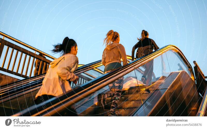 Women friends training running up escalator in city on sunset unrecognizable female group runner team women mechanic stair staircase step sunrise sunshine leg