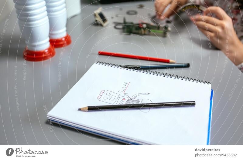 Robot draw by child on notebook and student assembling pieces of toy in a robotics class children female pencil colours paint doodle close up detail solar panel