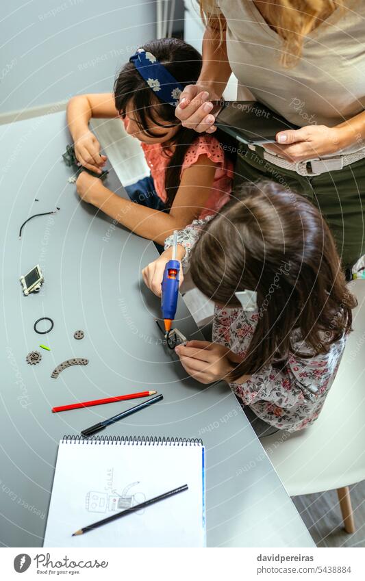 Students working with machine pieces next to teacher in robotics class unrecognizable student children female electronic circuit electrical concentrate helping