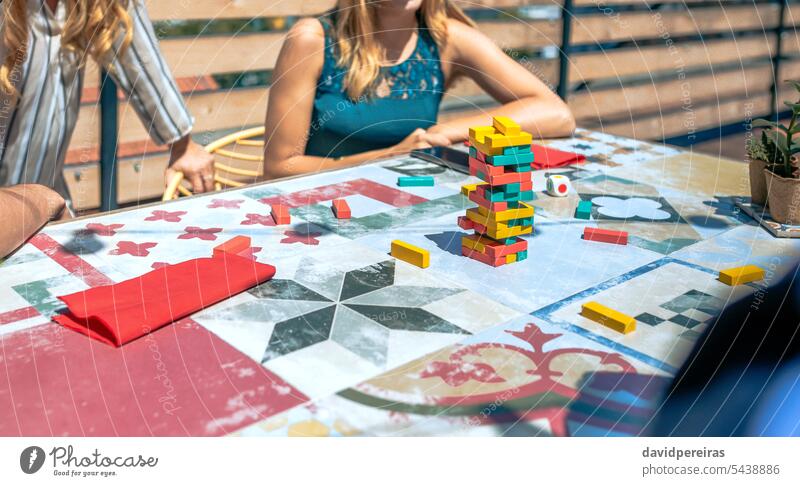 Jenga tower over table with unrecognizable people playing in a rooftop party jenga game piece block wood terrace tile construction structure board strategy