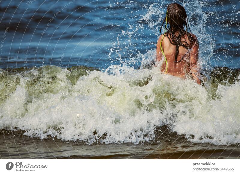 Little girl playing with waves in the sea. Kid playfully splashing with waves. Child jumping in sea waves. Summer vacation on the beach summer vacations ocean