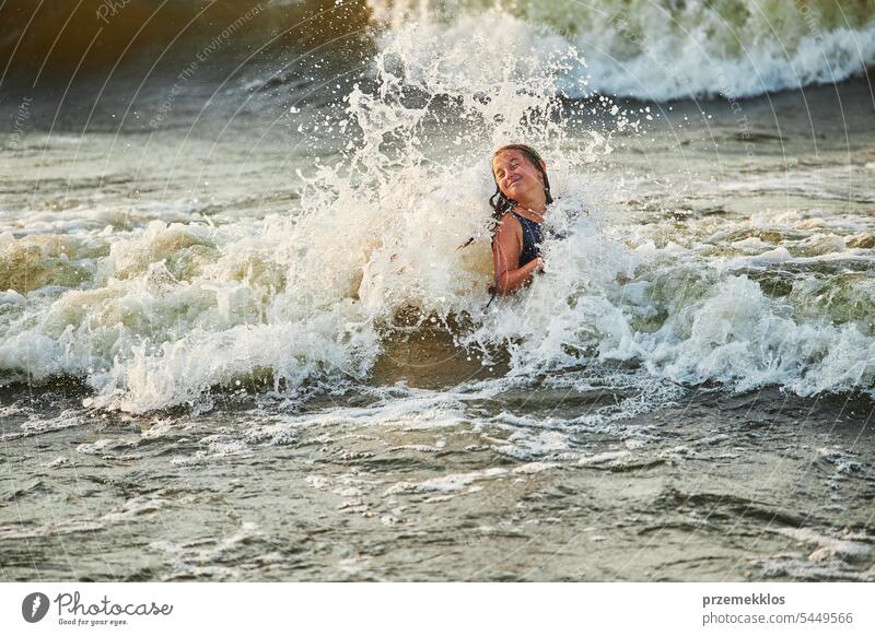 Little girl playing with waves in the sea. Kid playfully splashing with waves. Child jumping in sea waves. Summer vacation on the beach summer vacations ocean