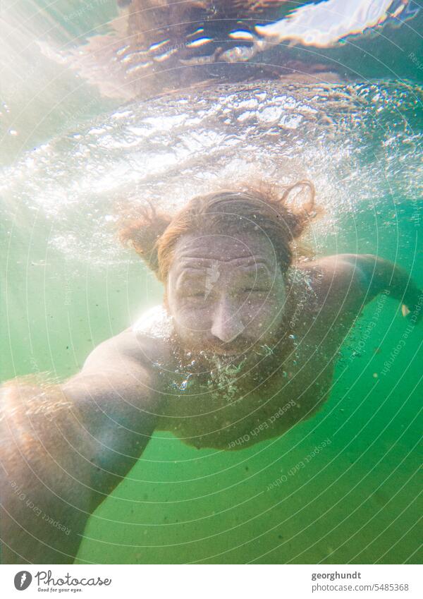 Man with red hair and red beard dives in a freshwater lake. Eyes open, but slightly squinted. He holds the camera. Lake underwater Dive be afloat bathe