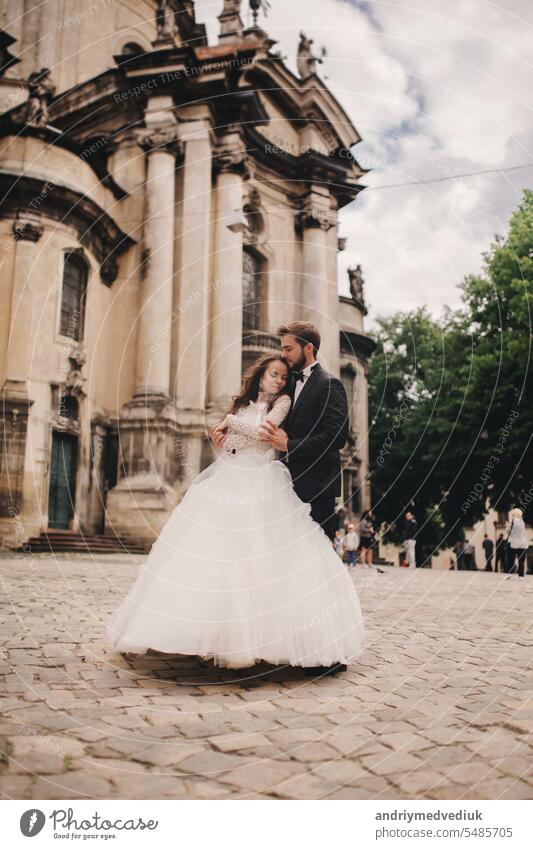 Stylish bride and groom gently hugging on european city street. Gorgeous wedding couple of newlyweds embracing near ancient building. romantic sensual moment of newlyweds