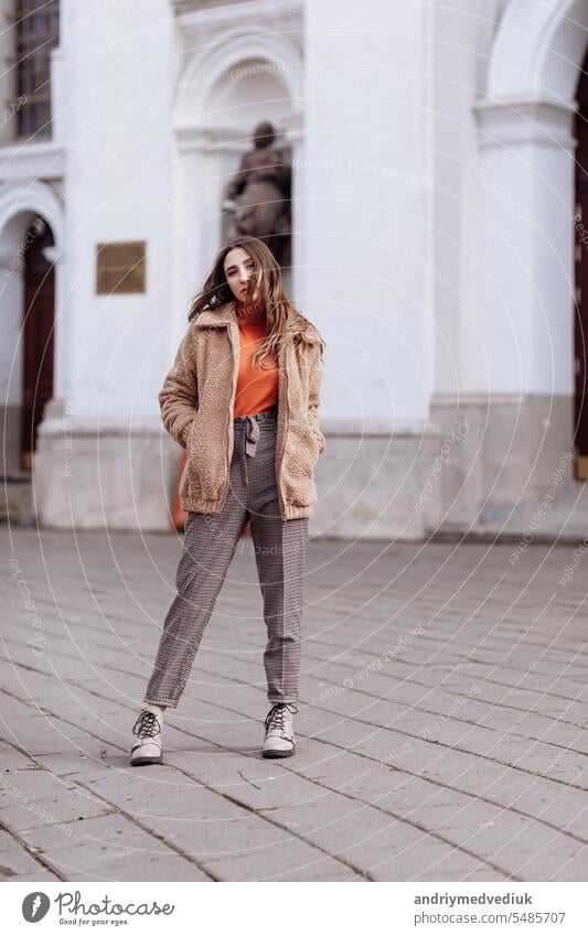 Fashion style portrait. beautiful stylish girl with long hair walks in the city. Portrait of attractive girl on the street. Spring or fall day. selective focus.