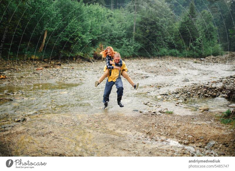 Couple in love - young hipster man is carrying his redhead woman on back near the river in the mountain couple fun girlfriend happy together happiness boyfriend