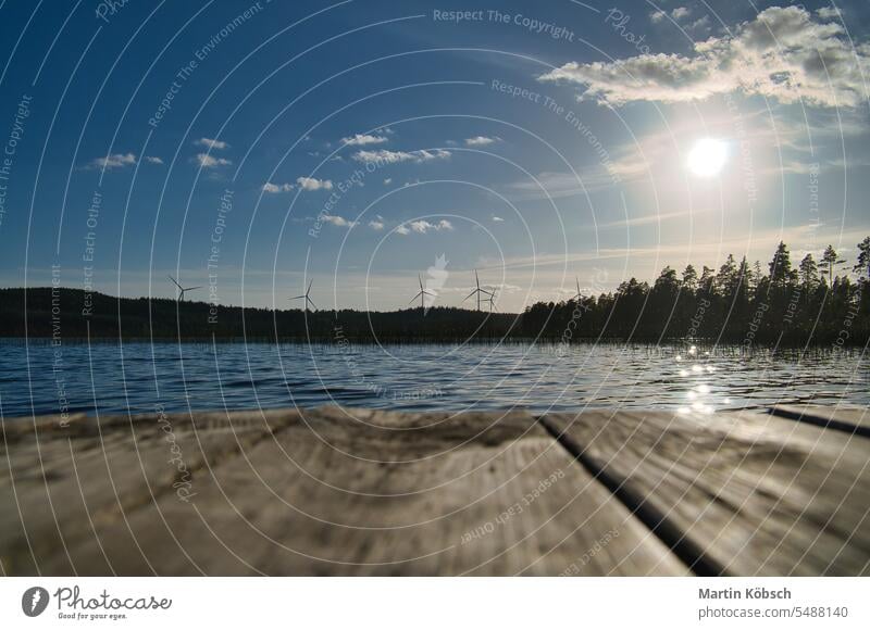 View over a footbridge into the blue water of a lake. Wind turbines in the background. Bathing evening beautiful wind turbines electricity renewable energy dusk