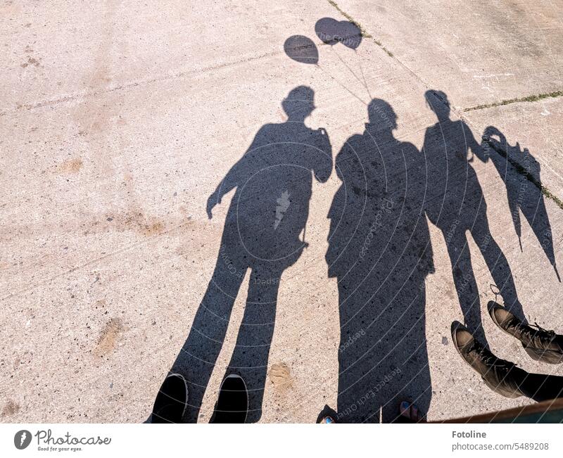 The shadows of three ladies on an ugly concrete path. Our shoes merge with the shadows. We had balloons and umbrellas with us as accessories. Shadow Silhouette