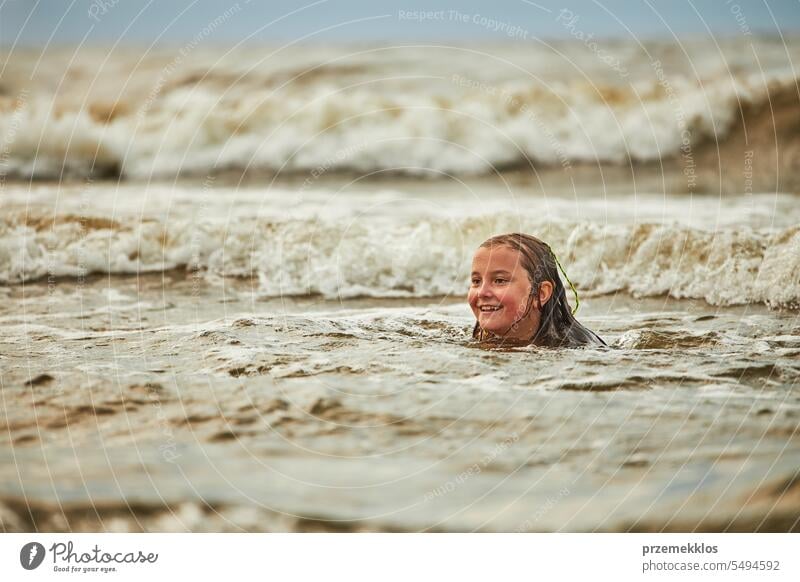 Little girl playing with waves in the sea. Kid playfully splashing in waves. Child jumping in sea. Vacations on the beach. Water splashes summer vacations ocean