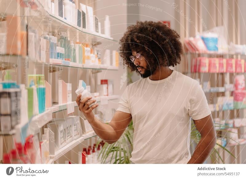 Black man with afro hairstyle reading label on bottle at pharmacy ingredient medicine drugstore buy customer package health care shop purchase information