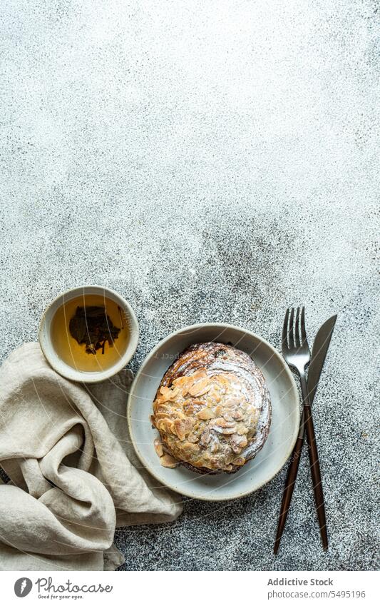 Sweet almond pastry on the plate with cup of green tea sweet fork knife dish surface table high angle from above food drink dessert eat yummy appetizing