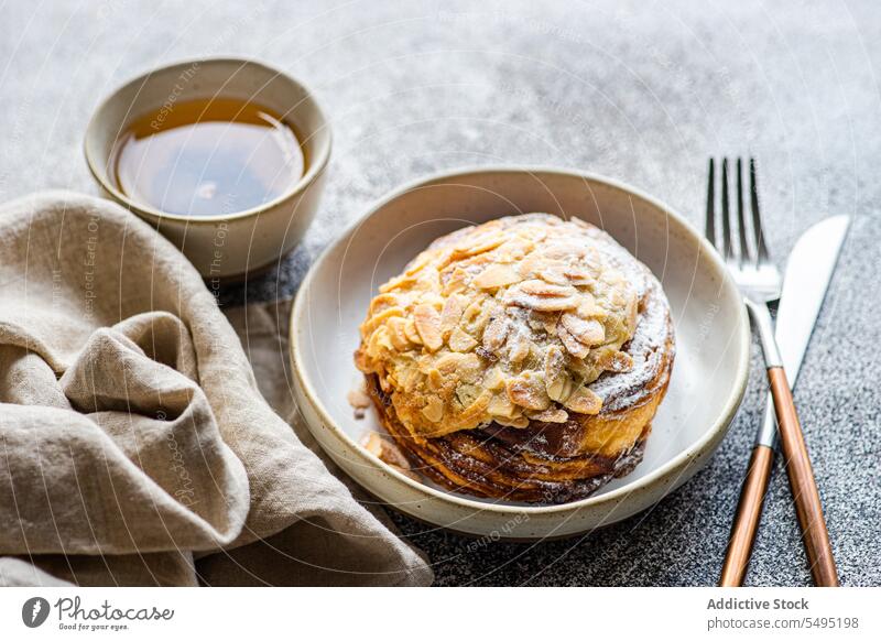 Sweet almond pastry on the plate with cup of green tea sweet fork knife dish surface table high angle from above food drink dessert eat yummy appetizing