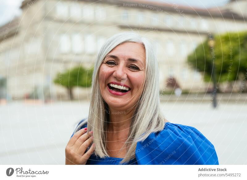 Smiling woman standing on city street positive smile happy glad cheerful optimist female modern delight joy satisfied elderly senior enjoy content pleasant town