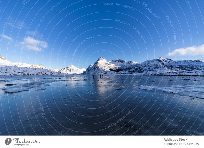 Travelers standing on frozen lake near snowy mountains traveler tourist winter nature lofoten island norway shore coast cold blue sky ice scenic north trip