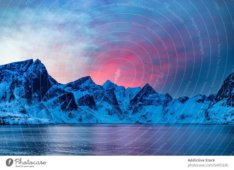 Snowy mountains near sea against cloudy sky at sunset seascape rocky ridge water formation sundown evening winter scenery snow cold freeze lofoten island norway