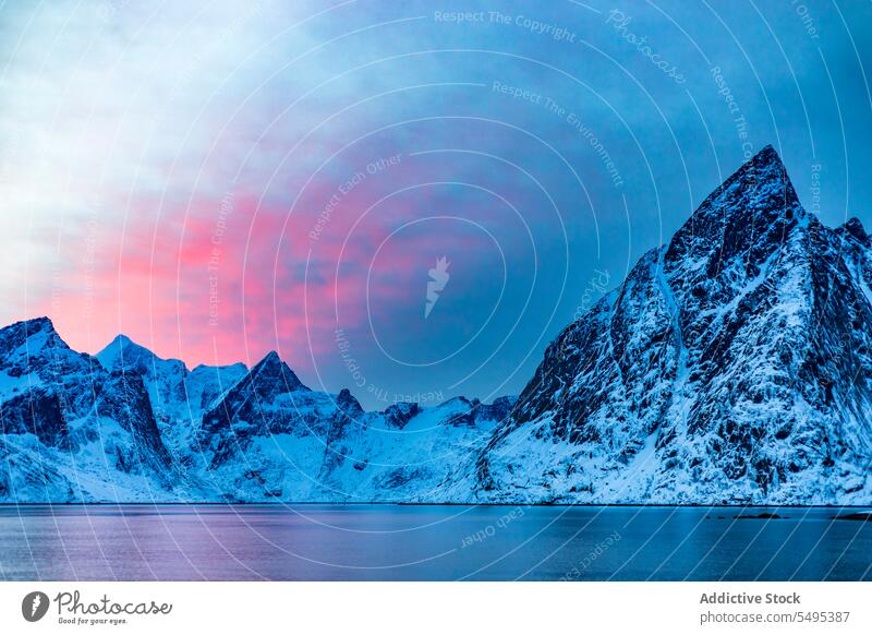 Snowy mountains near sea against cloudy sky at sunset seascape rocky ridge water formation sundown evening winter scenery snow cold freeze lofoten island norway