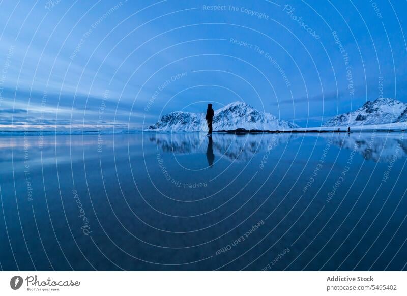 Traveler admiring lake near snowy mountains in winter traveler tourist sky nature island lofoten shore norway coast cold highland water scenic scenery