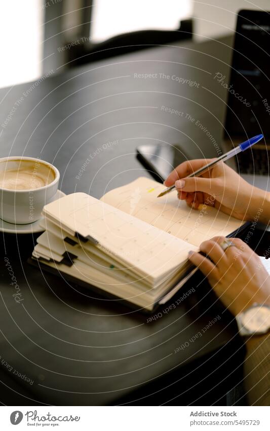 Unrecognizable young woman sitting at table and making notes in cafe take note write notebook notepad planner pen female positive free time cafeteria optimist