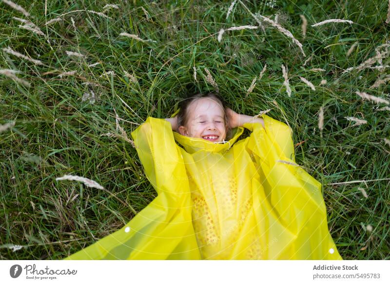 Little cute girl lying on green grass kid laugh nature happy meadow enjoy child having fun play little raincoat childhood positive content activity playful