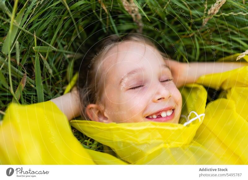 Little cute girl lying on green grass kid laugh nature happy meadow enjoy child having fun play little raincoat childhood positive content activity playful