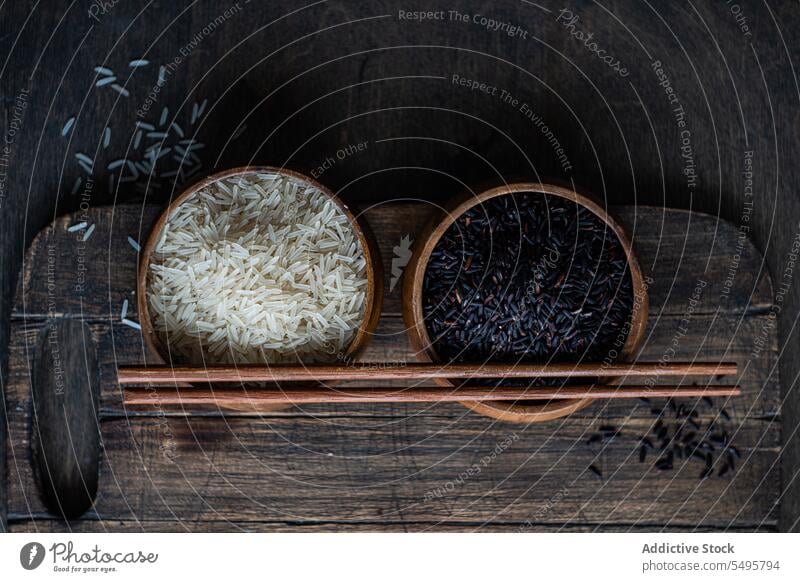 Raw wild black rice and peeled white rice in the bowls with chopsticks. raw table surface food served menu meal lunch dinner ingredient dish cuisine healthy